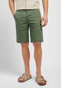 Gröna bomullsshorts med rak skärning, sidofickor och fållad finish. Matchas med beige sandaler med justerbara remmar.