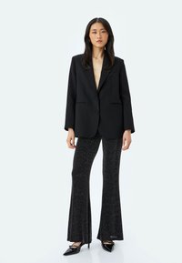 Zwarte op maat gemaakte blazer met een reverskraag, sluiting met één knoop en twee voorzakken, gecombineerd met strakke, sprankelende flared zwarte broek en hakken.