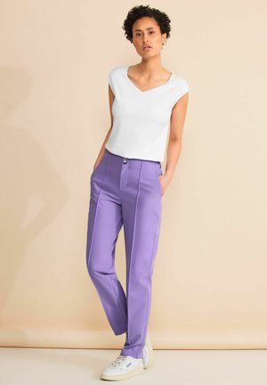 Witte top met korte mouwen en een V-hals, gecombineerd met lichtpaarse rechtzittende pantalons met zijzakken en een knoopsluiting. Witte sneakers.