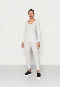 Top de manga comprida cinza claro e leggings coordenados feitos de material macio e elástico; design ajustado, combinado com ténis pretos.