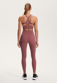 Bordo aktivna obleka, ki vključuje športni modrček z naramnicami in izrezanimi detajli ter visoke legice z gladko teksturo in prilagojenim krojem.