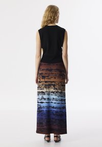 Zwarte mouwloze top met een ronde halslijn en een lange gradientrok met abstracte tekstpatronen in bruin, blauw en zwart.