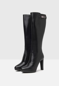 Black leather knee-high boots with a sleek design, high stiletto heels, smooth texture, and a subtle metallic hardware accent at the top.