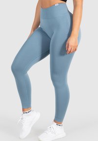 Leggings azzurri chiari realizzati in materiale elasticizzato, con vita alta, motivo testurizzato lungo il lato e abbinati a scarpe bianche.
