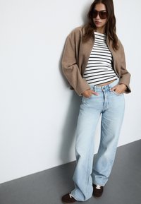 Kratka tan jakna preko črno-bele črtaste majice, v kombinaciji z svetlo modrimi širokimi kavbojkami in rjavimi semiš supergami.