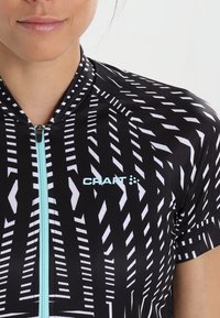 Jersey de ciclismo negro con un patrón geométrico blanco, mangas cortas, cierre frontal y un logo azul claro en el pecho.