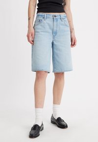 Svetlomodré denim šortky s rovným strihom, piatimi vreckami a zapínaním na gombík. Vytvorené s čiernymi mokasínami a bielymi ponožkami.