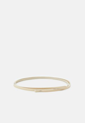 Dunne beige leren riem plat gelegd in een losse cirkel op een effen witte achtergrond.
