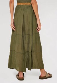 Falda maxi verde en capas, hecha de una tela ligera, con una cinturilla elástica texturizada y sandalias planas informales con un lazo decorativo.