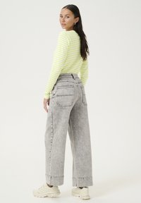 Langarm, nauwsluitend top in geel met witte strepen; hoge taille, wijde grijze denim jeans met achterzakken en uitgerafelde omslagen.