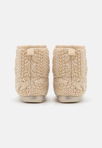 Gebreide beige pantoffels met een gestructureerd patroon, voorzien van een lusdesign en een zachte stofafwerking. Licht van gewicht met een tan kleurige zool.