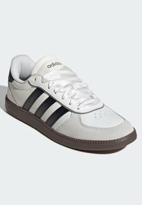Adidas sneakers featuring a white leather upper, three black stripes, rounded toe, and rubber outsole with textured accents.