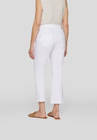 Weiße, cropped Jeans mit einem mittelhohen Bund, ausgestattet mit zwei Gesäßtaschen und einem ausgefransten Saum. Tragen Sie dazu braune Rutschsandalen.