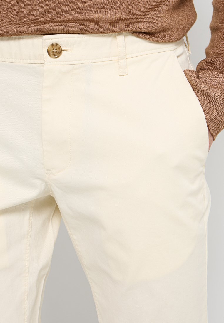 Pantalon en coton couleur crème avec une poche latérale, fermant par un bouton, avec une coupe droite et une texture lisse.