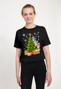 Černé tričko s potiskem zeleného vánočního stromku s barevnými ozdobami, třemi kreslenými medvědy a dárky, umístěné na zimním pozadí.