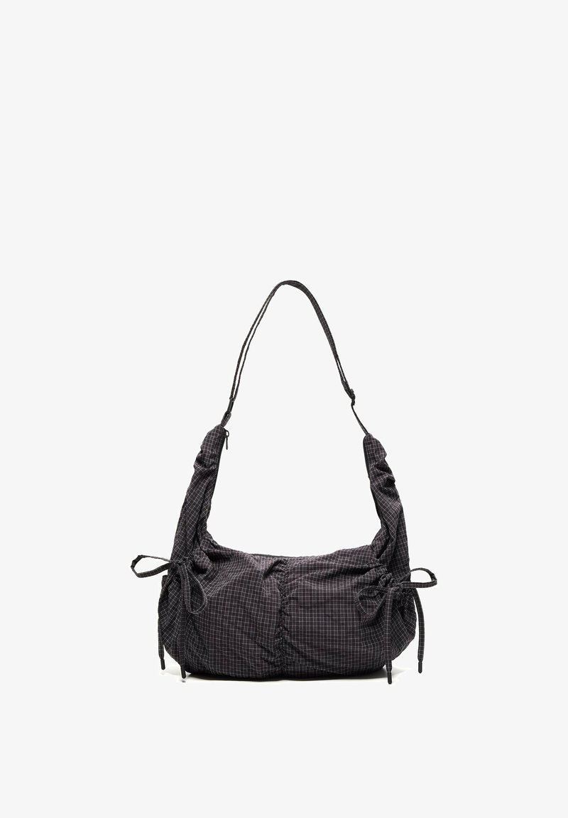 Sac à épaule en tissu noir avec motif à carreaux blancs, bandoulière réglable et cordons de serrage des deux côtés, sur fond blanc.