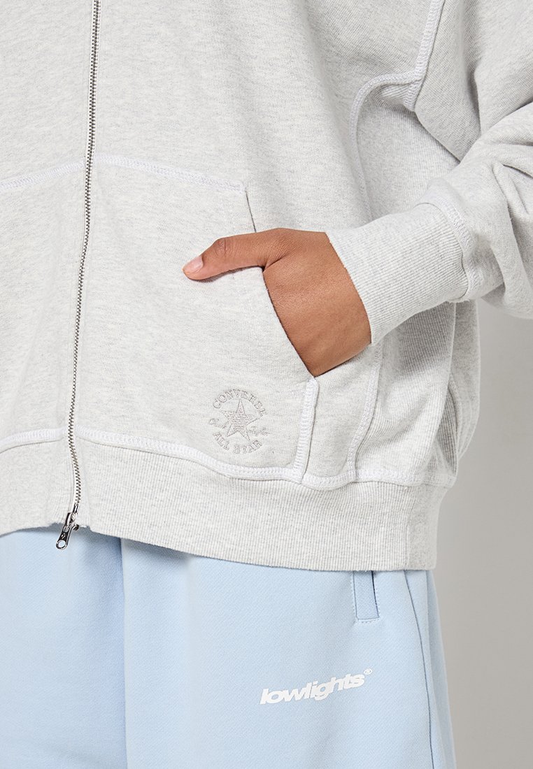 Grauer Zip-Hoodie aus weichem Baumwollgemisch, mit einer Fronttasche, gerippten Bündchen und einem dezenten, tonal gehaltenen Logo auf der Tasche.