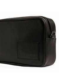 Caja rectangular de cuero negro con superficie texturizada, cierre de cremallera y parche con logo. Presenta bordes redondeados y un lazo lateral para sujeción.