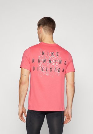 Homme vu de dos portant un t-shirt corail Nike avec un texte noir "Nike Running Division" et un motif léopard dans le dos, ainsi que des leggings noirs.