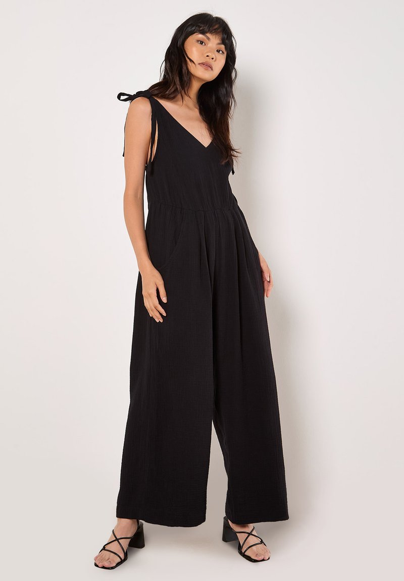 Black jumpsuit with a v-neckline, tie shoulder straps, loose legs, and pockets. Made of textured fabric for a relaxed fit.