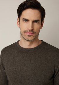 Brązowy, dziergany sweter z okrągłym dekoltem i długimi rękawami. Gładka faktura i dopasowany krój podkreślający kołnierz i mankiety.