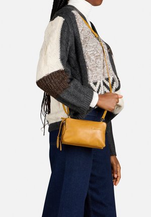 Borsa a tracolla in pelle tan con dettaglio zip, texture liscia e tracolla removibile, indossata con un maglione grigio e bianco a fantasia.