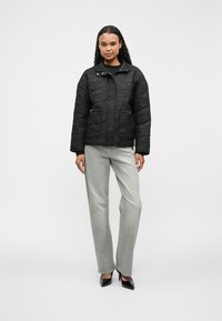 Čierna prešívaná bunda s golierom, predným zipsom a dvoma bočnými vreckami, kombinovaná so svetlo šedými nohavicami rovného strihu a čiernymi lodičkami.