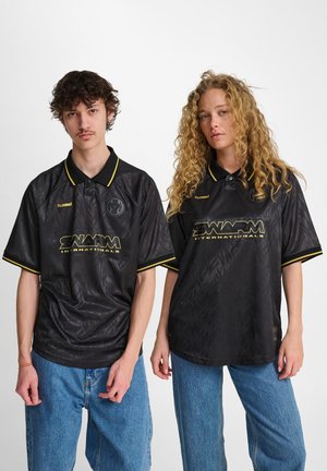 Black short-sleeve polo shirts with textured pattern, yellow accents at collar and sleeves, branded logo on chest. Worn with blue jeans.