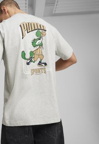 Lichtgrijs katoenen T-shirt met een groene cartoonpersonage dat een basketbal dribbelt op de achterkant, met de tekst "PUMA" en "SPORTS TECHNIQUE".