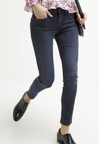 Jeans skinny de mezclilla azul oscuro con una textura suave. Presenta una cintura baja, diseño clásico de cinco bolsillos y un ligero estiramiento para un mejor ajuste.