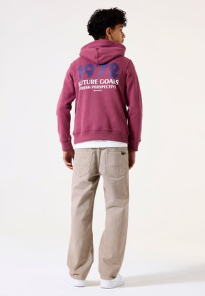 Bordeaux hoodie met witte en blauwe graphics met de tekst "FUTURE GOALS FRESH PERSPECTIVE 1972," gecombineerd met beige broek en witte sneakers.
