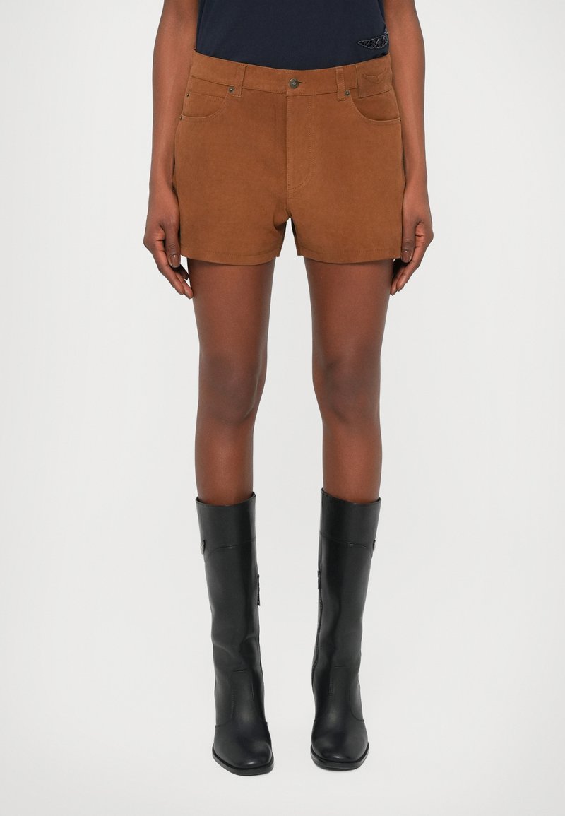Shorts en daim marron avec deux poches avant et des coutures latérales, associés à des bottes en cuir noir montantes, avec une texture lisse et un bout arrondi.