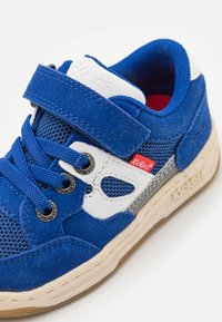 Kék velúr és hálós sneaker fehér kiegészítőkkel, szürke részletekkel és tépőzárral. Laposszálú fűzővel és világosbarna gumitalppal rendelkezik.
