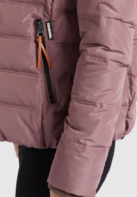 Vadderad jacka i mauve med en dragkedjefack med orange dragflik. Slät, glänsande textur med horisontell sömnadsdetalj.