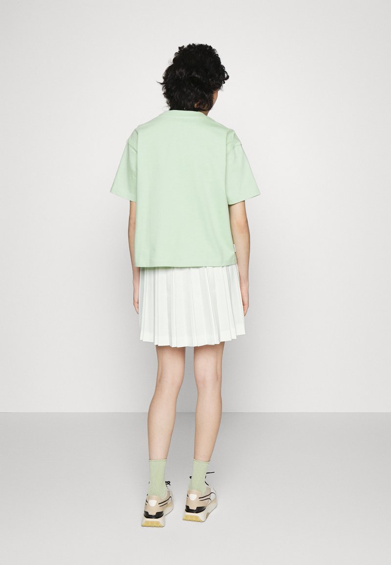 Mintgrünes Baumwoll-T-Shirt mit kurzen Ärmeln, kombiniert mit einem weißen plissierten Rock, mintgrünen Socken und klobigen Sneakern mit neutralen Akzenten.