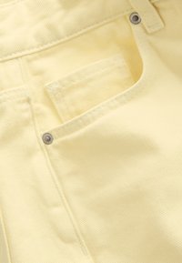 Pantalon en velours côtelé jaune avec poche avant, détail de rivet métallique et tissu texturé, mettant en avant la douceur et les coutures durables.
