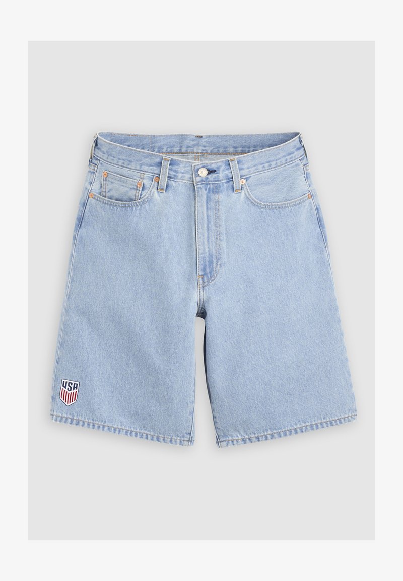 Shorts vaqueros azul claro con bolsillos delanteros, trabillas para cinturón, cierre de botón y un pequeño parche con escudo de EE. UU. en la pierna izquierda.