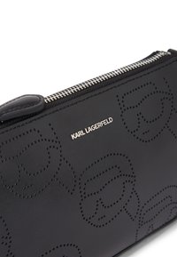 Portafoglio in pelle nera con design embossati e un logo argentato. Ha una texture liscia con chiusura a zip nella parte superiore.