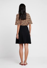 Blouse à imprimé léopard marron avec des manches courtes, associée à une jupe noire évasée. L'ensemble présente un tissu texturé et une taille cintrée.