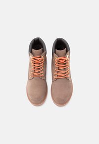 Botas de camurça castanha com gola acolchoada preta, atacadores laranjas e solas de borracha. Apresenta uma textura suave e design clássico.