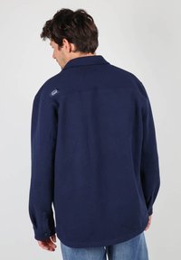 Chemise en polaire bleu marine avec un col, des poignets boutonnés et des détails de couture au dos. Présente un petit logo de marque sur l'épaule gauche.