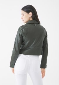 Mörkgrön läderjacka med en kortad design och krage. Har sömnadsdetaljer och tryckknappsstängning på baksidan. Bärs med vita jeans.