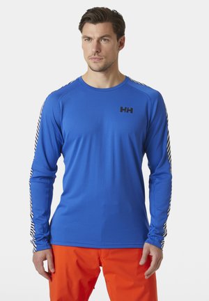 Langsleeve, blauwe sportshirt van textuurstof. Heeft een zwart logo op de borst en gestreepte accenten op de mouwen.