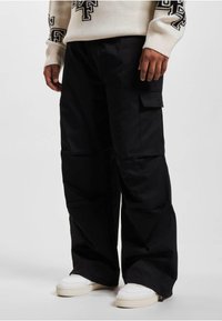 Sorte cargo bukser med en afslappet pasform, der har sidelommer, en glat tekstur og et bredt ben-design. Båret med hvide sneakers.