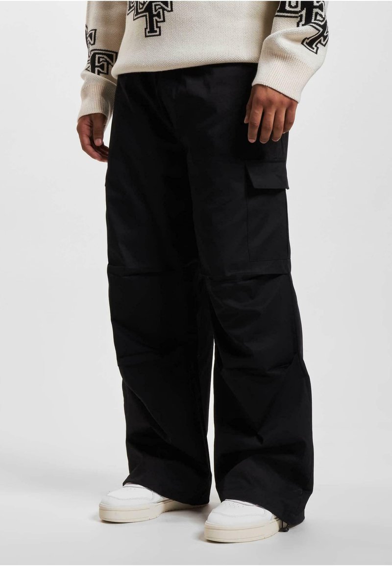 Sorte cargo bukser med en afslappet pasform, der har sidelommer, en glat tekstur og et bredt ben-design. Båret med hvide sneakers.