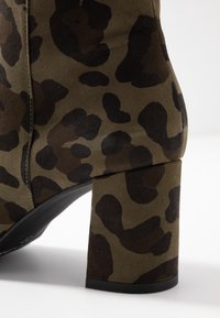 Hnědo-černé leopardí vzorované semišové kotníkové boty s širokým blokovým podpatkem na bílém pozadí.