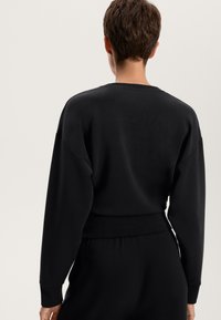 Felpa nera con scollatura rotonda, spalle scese e polsini a costina. Tessuto morbido con un aspetto leggermente texturizzato.