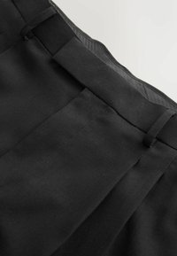 Black pleated trousers with a flat waistband, featuring a smooth texture and subtle stitching details, showcasing a classic design.