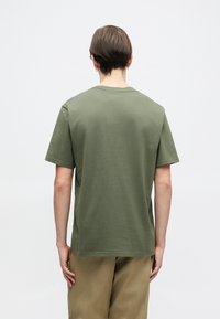 Olivově zelené tričko s krátkým rukávem z měkké bavlny, s klasickým kulatým výstřihem a uvolněným střih, vyznačující se minimalistickým designem.