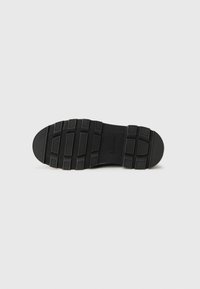 Semelle de chaussure en caoutchouc noir avec une surface texturée, présentant un design de semelle à motif et une empreinte de logo, adaptée pour l'adhérence et la durabilité.